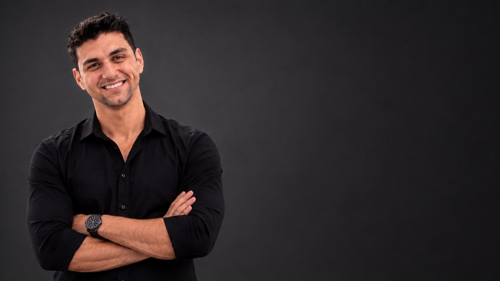 Bruno Alvarenga, psicólogo clínico, sorrindo, de braços cruzados e camisa social preta
